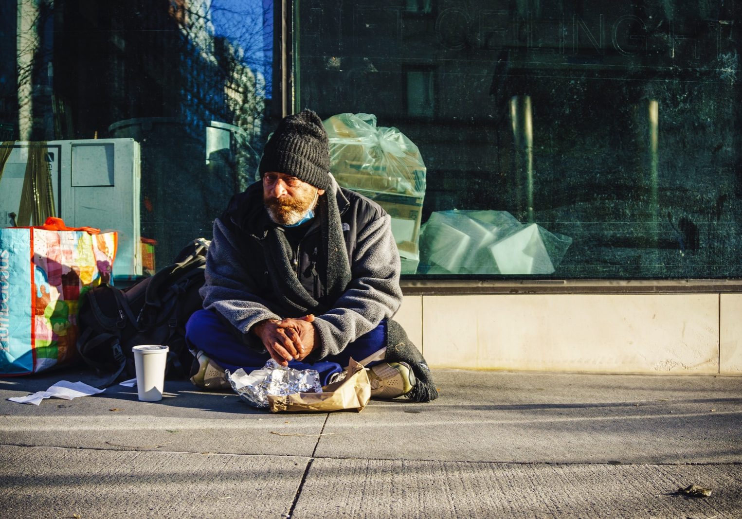 man in black and gray jacket sitting on sidewalk during daytime